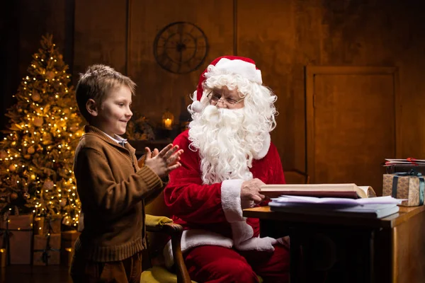 Noel Baba Küçük Çocuk Neşeli Noel Baba Masada Otururken Çalışıyor — Stok fotoğraf