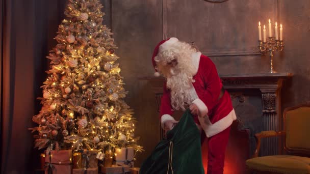 Lugar de trabajo de Santa Claus. Alegre Santa está trabajando mientras está sentado a la mesa. Chimenea y árbol de Navidad en el fondo. Concepto de Navidad. — Vídeos de Stock