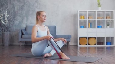 Spor giyim sektöründe genç ve sportif bir kız iç mekanda egzersiz yaparken direniş bandı kullanıyor. Formda ve narin sarışın kadın spor ve spor için geliyor. Sağlık sigortası, yağ yakma ve sağlık..
