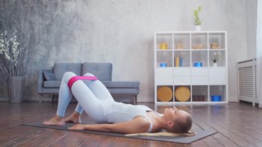 Spor giyim sektöründe genç ve sportif bir kız iç mekanda egzersiz yaparken direniş bandı kullanıyor. Formda ve narin sarışın kadın spor ve spor için geliyor. Sağlık sigortası, yağ yakma ve sağlık..