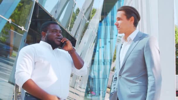 Уверенный афроамериканский бизнесмен и его коллега перед современным офисным зданием. Финансовые инвесторы говорят на открытом воздухе. Банковское дело. — стоковое видео
