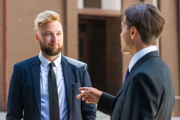 Homme d'affaires confiant et son collègue devant un immeuble de bureaux moderne. Les investisseurs financiers parlent en plein air. Banques et entreprises. — Photo