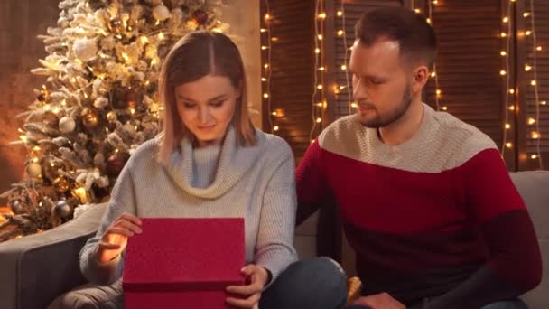 Pareja joven y cariñosa celebrando la Navidad en casa. Joven y su novia en el interior de una casa con un árbol de Navidad en el fondo. — Vídeos de Stock