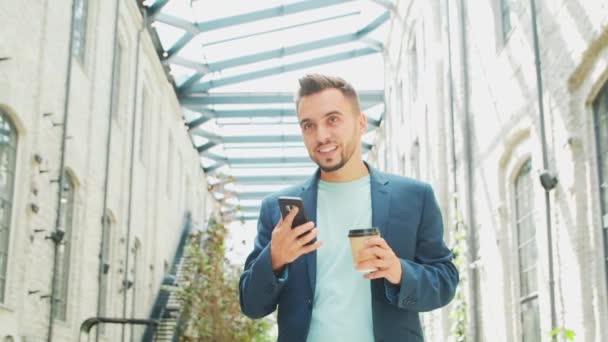 Um jovem empresário bem sucedido está trabalhando ao ar livre usando o smartphone. Um homem de fato casual. Trabalho de negócios, freelance e remoto. — Vídeo de Stock