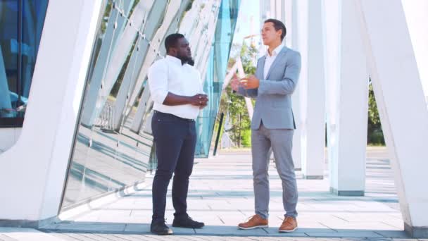 Empresário afro-americano confiante e seu colega em frente ao edifício de escritórios moderno. Os investidores financeiros estão a falar ao ar livre. Banca e negócios. — Vídeo de Stock