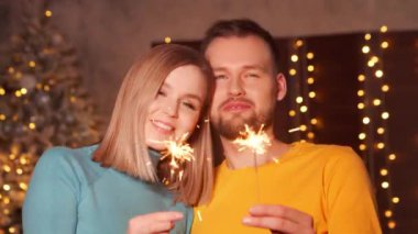 Genç ve sevgi dolu bir çift Noel 'i evde maytaplarla kutluyor. Genç adam ve kız arkadaşı arka planda Noel ağacı olan bir evde..