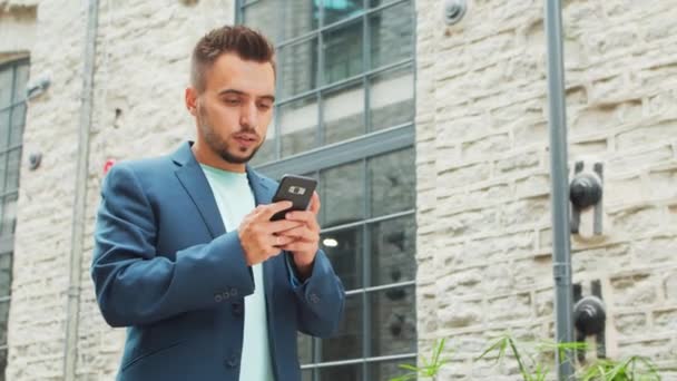 Un joven empresario exitoso está trabajando al aire libre con un teléfono inteligente. Un hombre con ropa casual. Negocios, freelance y trabajo remoto. — Vídeos de Stock