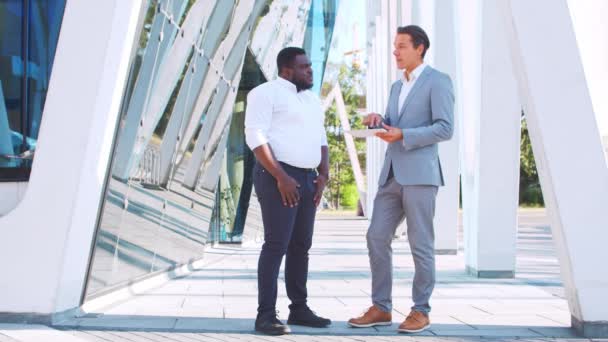 Un hombre de negocios afroamericano confiado y su colega frente al moderno edificio de oficinas. Los inversores financieros están hablando al aire libre. Banca y negocios. — Vídeo de stock