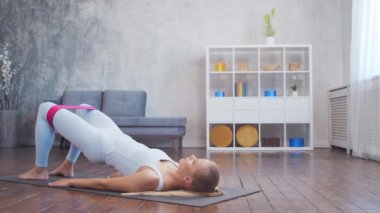 Spor giyim sektöründe genç ve sportif bir kız iç mekanda egzersiz yaparken direniş bandı kullanıyor. Formda ve narin sarışın kadın spor ve spor için geliyor. Sağlık sigortası, yağ yakma ve sağlık..