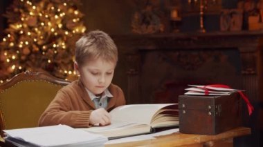 Küçük çocuk masada otururken sihirli bir kitap okur. Noel ağacı ve şöminesi olan bir ev. Noel konsepti.