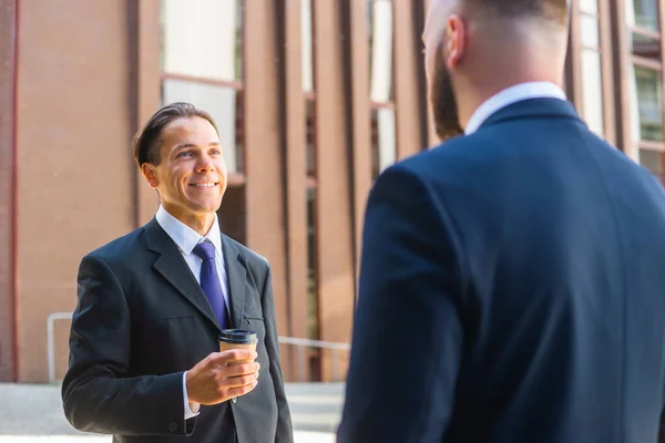 Homme d'affaires confiant et son collègue devant un immeuble de bureaux moderne. Les investisseurs financiers parlent en plein air. Banques et entreprises. — Photo