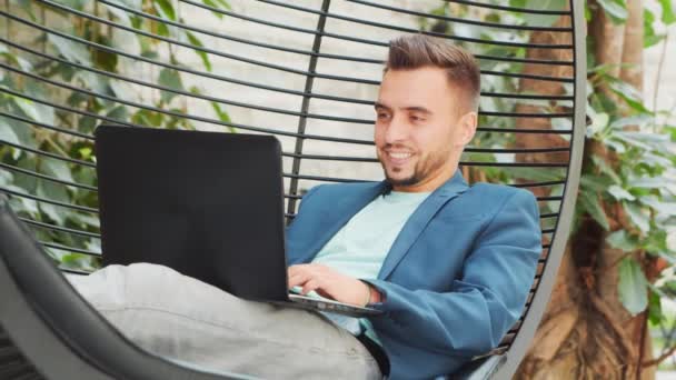 En ung, suksessfull forretningsmann jobber i et salong med en datamaskin. Forretninger, frilanser og fjernarbeid. – stockvideo
