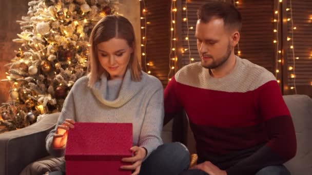 年轻夫妇在家里庆祝圣诞节.一个年轻的男人和他的女朋友在一个家庭内部，背景上有一棵圣诞树. — 图库视频影像