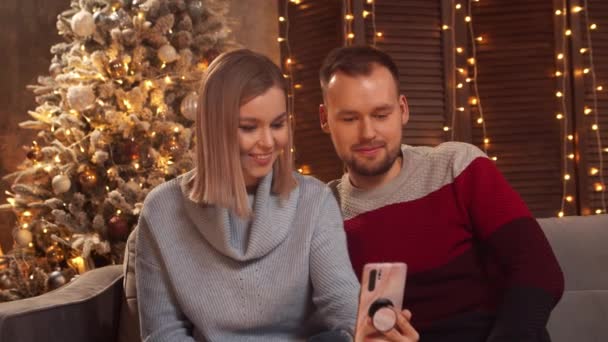 Молодая любящая пара празднует Рождество дома. Молодой человек и его девушка в интерьере дома с елкой на заднем плане. — стоковое видео