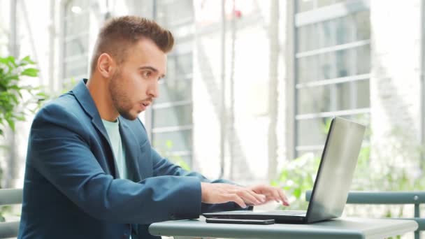 Młody, odnoszący sukcesy biały biznesmen pracuje w kawiarni na zewnątrz przy użyciu komputera. Biznes, praca na własny rachunek i praca zdalna. — Wideo stockowe