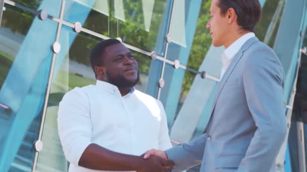 Un hombre de negocios afroamericano confiado y su colega frente al moderno edificio de oficinas. Los inversores financieros están hablando al aire libre. Banca y negocios. — Vídeos de Stock