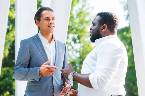 African-American businessman and his colleague in front of modern office building. Financial investors are talking outdoor. Banking and business concept. — Stock Photo, Image