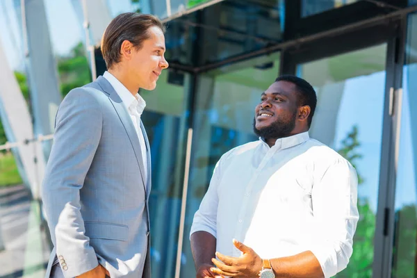 Afroamerikansk affärsman och hans kollega framför en modern kontorsbyggnad. Finansiella investerare pratar utomhus. Bank- och affärsidé. — Stockfoto