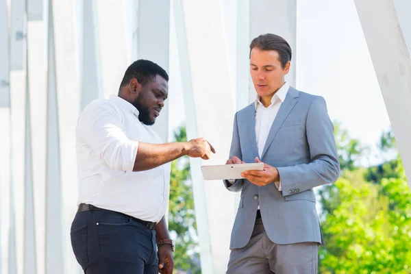 African-American businessman and his colleague in front of modern office building. Financial investors are talking outdoor. Banking and business concept. — Stock Photo, Image
