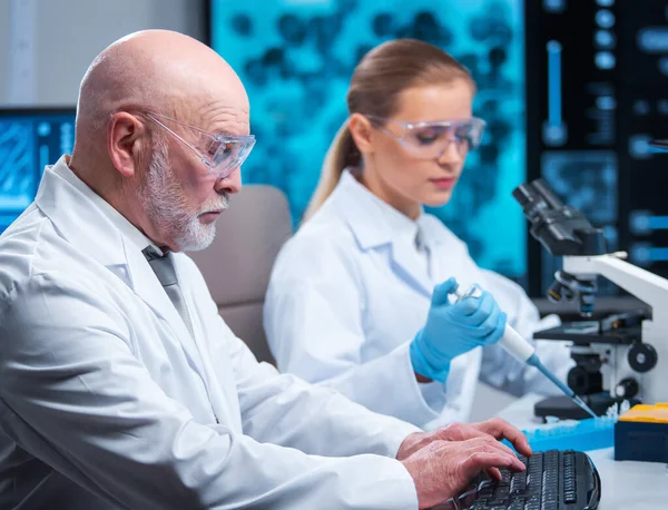 Ο καθηγητής και ο γιατρός εργάζονται σε ένα σύγχρονο επιστημονικό εργαστήριο χρησιμοποιώντας εξοπλισμό και τεχνολογίες πληροφορικής. Ομάδα επιστημόνων κάνουν έρευνα και αναπτύσσουν νέα εμβόλια. Επιστήμη και υγειονομική περίθαλψη. — Φωτογραφία Αρχείου