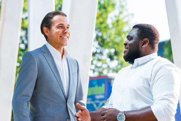 Hombre de negocios afroamericano y su colega frente al moderno edificio de oficinas. Los inversores financieros están hablando al aire libre. Concepto bancario y empresarial. — Foto de Stock