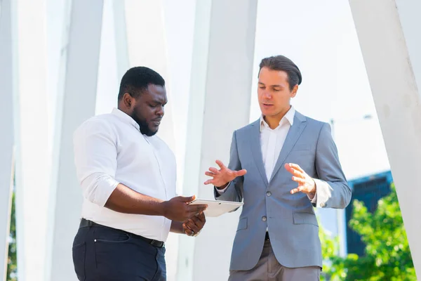 Der afroamerikanische Geschäftsmann und sein Kollege vor einem modernen Bürogebäude. Finanzinvestoren reden im Freien. Bank- und Geschäftskonzept. — Stockfoto