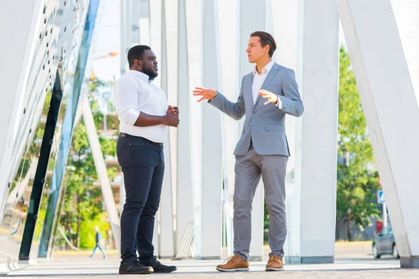 アフリカ系アメリカ人のビジネスマンや近代的なオフィスビルの前で彼の同僚。金融投資家は屋外で話している。銀行業務の概念. — ストック写真