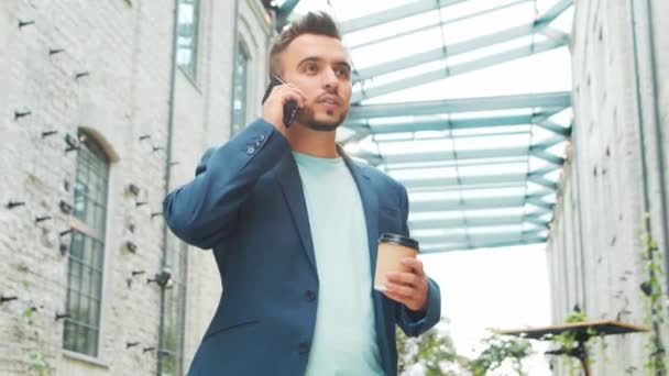 Un joven empresario exitoso está trabajando al aire libre con un teléfono inteligente. Un hombre con ropa casual. Negocios, freelance y trabajo remoto. — Vídeos de Stock