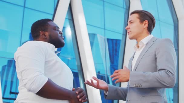 Empresário afro-americano confiante e seu colega em frente ao edifício de escritórios moderno. Os investidores financeiros estão a falar ao ar livre. Banca e negócios. — Vídeo de Stock