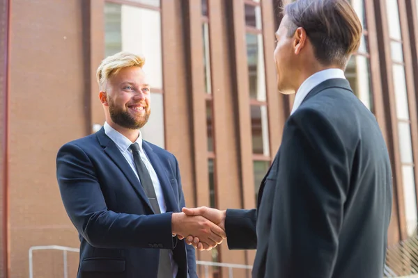 L'uomo d'affari fiducioso e il suo collega stanno stringendo la mano di fronte al moderno edificio per uffici. Investitori finanziari all'aperto. Settore bancario e commerciale. — Foto Stock