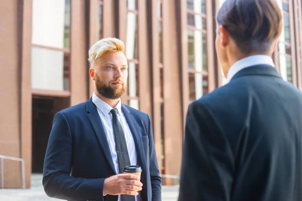 Homme d'affaires confiant et son collègue devant un immeuble de bureaux moderne. Les investisseurs financiers parlent en plein air. Banques et entreprises. — Photo