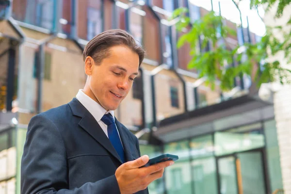 近代的なオフィスビルの前でビジネスマンを自信を持って。金融投資家はスマートフォンを屋外で使用しています。銀行業. — ストック写真