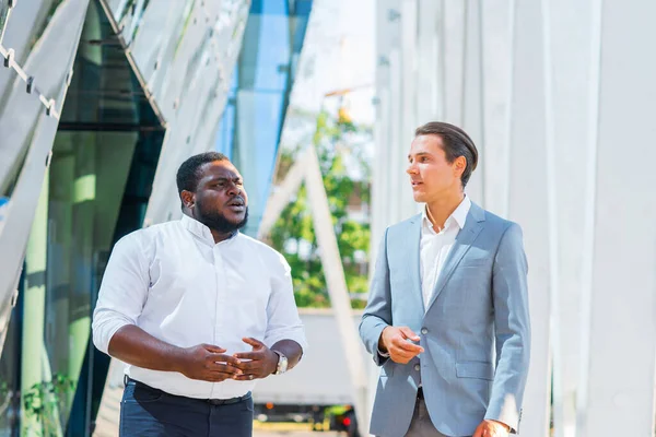 アフリカ系アメリカ人のビジネスマンや近代的なオフィスビルの前で彼の同僚。金融投資家は屋外で話している。銀行業務の概念. — ストック写真