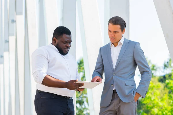 African-American businessman and his colleague in front of modern office building. Financial investors are talking outdoor. Banking and business concept. — Stock Photo, Image