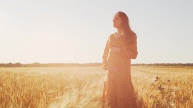 Günbatımında hamile bir kadın. Güzel bir genç kız bir çocuğun doğmasını umarak tarlada yürüyor. Annelik ve hamilelik kavramı.