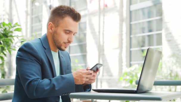 Joven exitoso hombre de negocios caucásico trabaja en un café al aire libre con una computadora. Negocios, freelance y trabajo remoto. — Vídeos de Stock