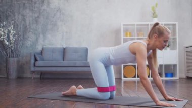 Spor giyim sektöründe genç ve sportif bir kız iç mekanda egzersiz yaparken direniş bandı kullanıyor. Formda ve narin sarışın kadın spor ve spor için geliyor. Sağlık sigortası, yağ yakma ve sağlık..