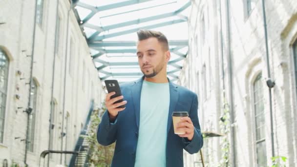 Um jovem empresário bem sucedido está trabalhando ao ar livre usando o smartphone. Um homem de fato casual. Trabalho de negócios, freelance e remoto. — Vídeo de Stock