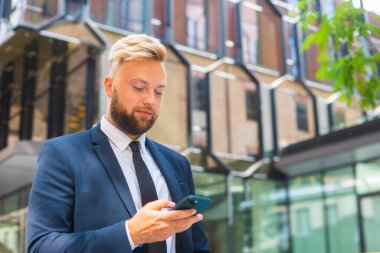 Modern ofis binasının önünde kendinden emin bir iş adamı. Finansal yatırımcı açık havada akıllı telefon kullanıyor. Bankacılık ve iş.