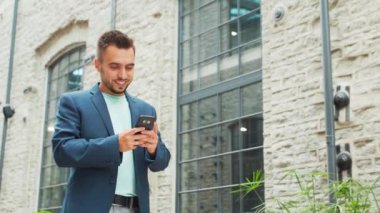 Genç ve başarılı bir iş adamı akıllı telefon kullanarak dışarıda çalışıyor. Sıradan giysili bir adam. İş, serbest meslek ve uzak çalışma.