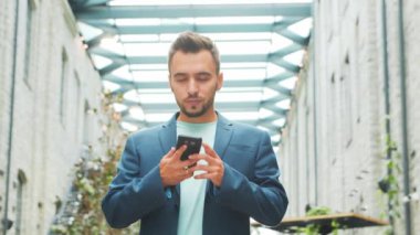 Genç ve başarılı bir iş adamı akıllı telefon kullanarak dışarıda çalışıyor. Sıradan giysili bir adam. İş, serbest meslek ve uzak çalışma.