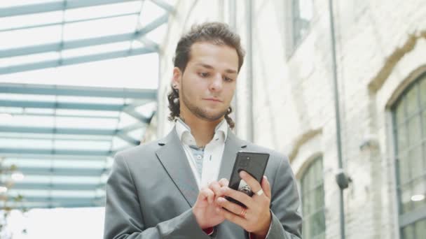 Un joven empresario exitoso está trabajando al aire libre con un teléfono inteligente. Un hombre con ropa casual. Negocios, freelance y trabajo remoto. — Vídeos de Stock