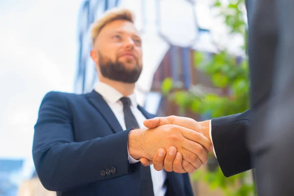 Handshake close-up. Businessman and his colleague are shaking hands in front of modern office building. Financial investors outdoor. Banking and business.