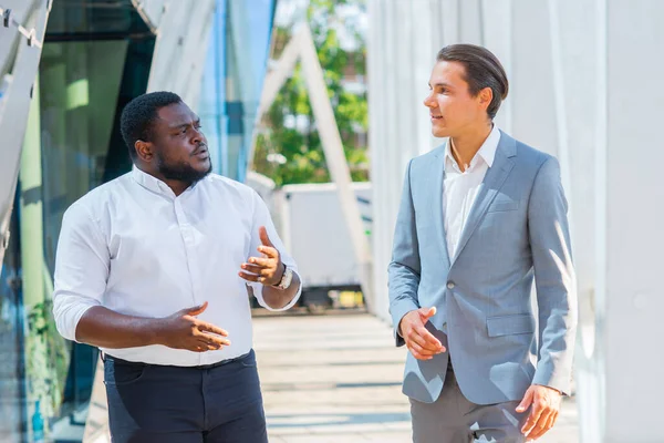 Homme d'affaires afro-américain et son collègue devant un immeuble de bureaux moderne. Les investisseurs financiers parlent en plein air. Concept bancaire et commercial. — Photo