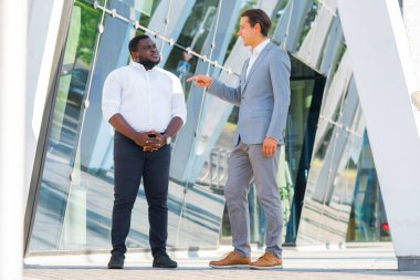 Modern ofis binasının önünde Afro-Amerikalı iş adamı ve meslektaşı. Finansal yatırımcılar dışarıda konuşuyorlar. Bankacılık ve iş konsepti.