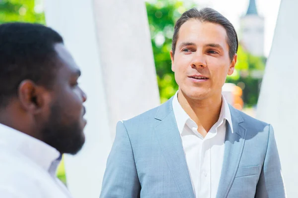 Homme d'affaires afro-américain et son collègue devant un immeuble de bureaux moderne. Les investisseurs financiers parlent en plein air. Concept bancaire et commercial. — Photo