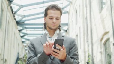 Genç ve başarılı bir iş adamı akıllı telefon kullanarak dışarıda çalışıyor. Sıradan giysili bir adam. İş, serbest meslek ve uzak çalışma.