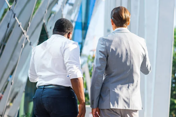 Afro-americký podnikatel a jeho kolega před moderní kancelářskou budovou. Finanční investoři mluví venku. Bankovní a podnikatelský koncept. — Stock fotografie