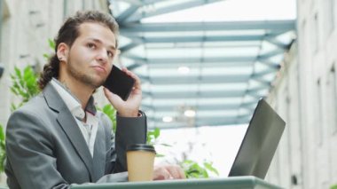 Genç başarılı beyaz iş adamı bir açık kafede bilgisayar ve akıllı telefon kullanarak çalışıyor. İş, serbest meslek ve uzak çalışma.