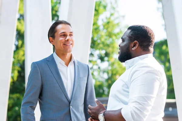 Афроамериканский бизнесмен и его коллега перед современным офисным зданием. Финансовые инвесторы говорят на открытом воздухе. Банковская и бизнес-концепция. — стоковое фото